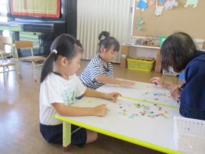 保育室で地域の方におはじきを教えてもらう子ども